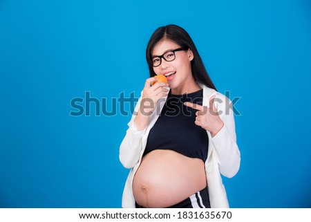 Beautiful pregnant woman in Asia is holding an orange in her hand. On a pink background, expectation of a young mother, pregnancy and childbirth pictures.
