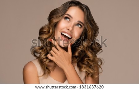Beautiful smiling woman holding hands near face and  looking to the side  . Beauty girl  with curly hair   . Presenting your product. Expressive facial expressions