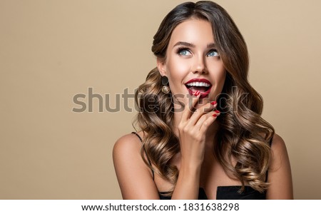 Shocked and surprised girl  smiling  looking to the side presenting  your product . Beautiful curly hair woman amazed ,   with red nails manicure. Expressive facial expressions. Pin up