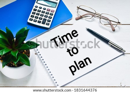 A calculator, glasses, a green plant lie next to a pen and a notebook with the words TIME TO PLAN. Flat lay.