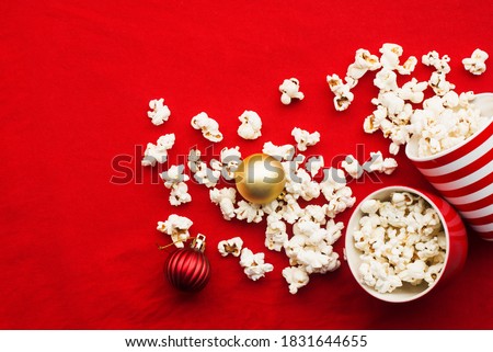 Homemade popcorn for a festive treat in red Christmas mugs with shiny New Year's red and gold Christmas decorations balls. Top view. Festive atmosphere picture. Top view