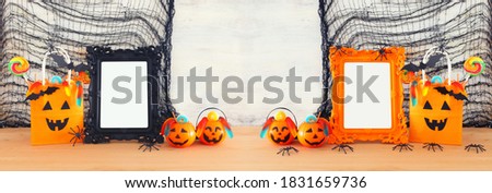 holidays image of Halloween. Pumpkins, bats, treats, paper gift bag next to empty photo frame for mockup over wooden table. for photography montage
