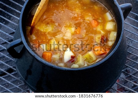 Stew cooked on fire outdoors in a cast-iron pot on a grill grid