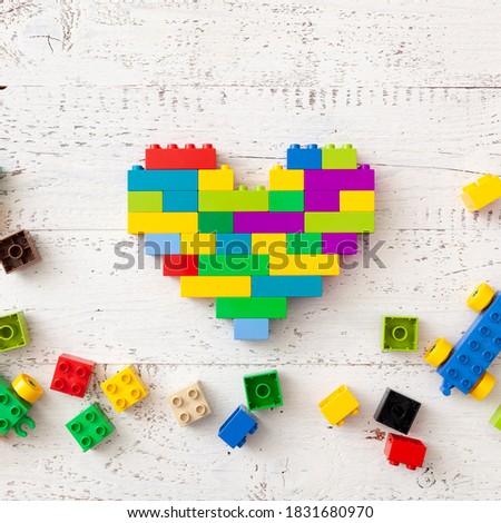 Multi-colored plastic cubes are scattered on a white wooden table. Creative building in the shape of a heart from a bright constructor. Early learning. Educational toys
