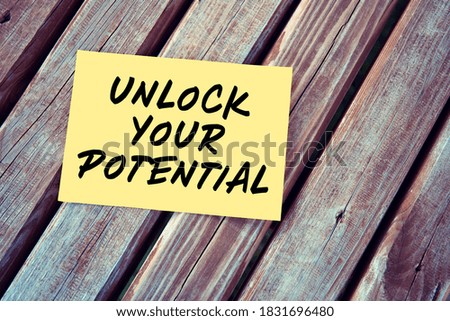Unlock your potential. Motivational or inspirational quote handwritten on yellow paper on a wooden table.