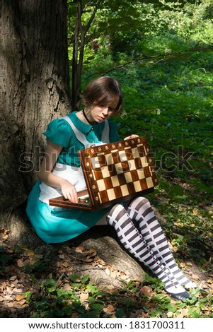 Alice in wonderland. A girl with a chessboard sits under a huge tree.