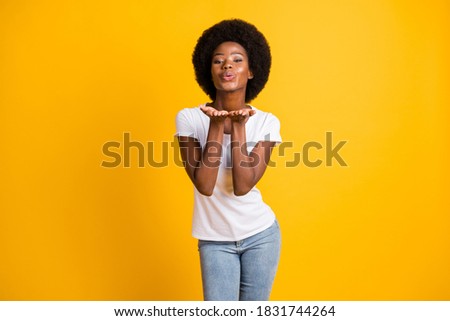 Photo portrait of young african american woman blowing you a kiss for valentine's day wearing white t-shirt isolated on vivid yellow colored background