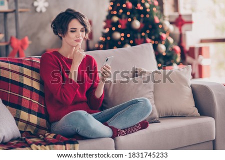 Full size photo of creative girl sit couch use smartphone think in house indoors with x-mas christmas atmosphere decoration