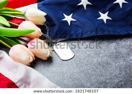 America United States flag and chain dog tags and tulip flower, military symbolizing, studio shot on concrete board background, US Veterans or Independence day concept