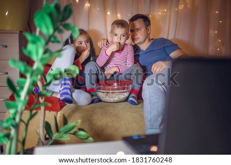 Family horror movie night. Father with kids sitting on couch and watching movie with popcorn by laptop at home, family entertainment, happy time together, childhood and entertainment, indoor lifestyle