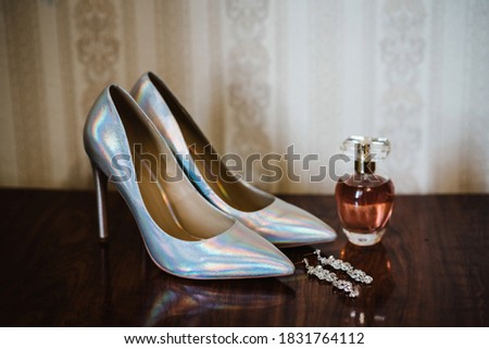 Stylish classic lacquered silver shoes, perfume, an earring on wooden background. Close up.