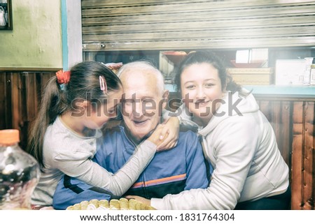 Elderly man celebrates birthday hugged by his nephews at home. Family concept, fast moving subjects.