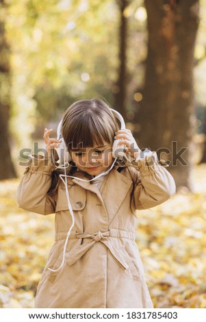 Portrait of a happy little girl listening to music on headphones in the autumn park
