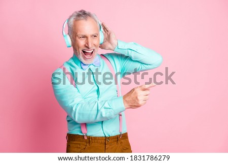Portrait photo of happy grandfather listening to music with headphones singing song pointing with finger isolated on pink color background