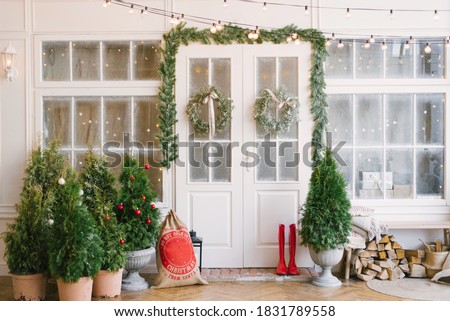 Porch with a white door in Christmas decorations and Christmas trees. Spruce garlands around the door. Beautiful winter terrace of the house with garlands of retro light bulbs Royalty-Free Stock Photo #1831789558