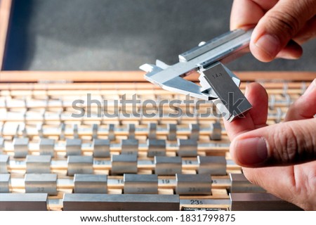 The inspector is calibrating a vernier caliper micrometer with a gauge block. A small number of gauge blocks can be used to create accurate lengths within a wide range. Royalty-Free Stock Photo #1831799875