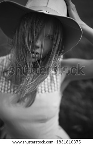Black and white portrait of a beautiful young woman wearing a summer dress and a sun hat, standing outdoors in a wheat field