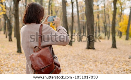 woman taking photo in autumn park, back view