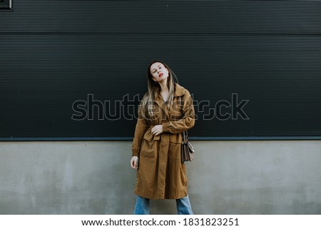 fashion and stylish blonde woman in winter coat posing behind black wall