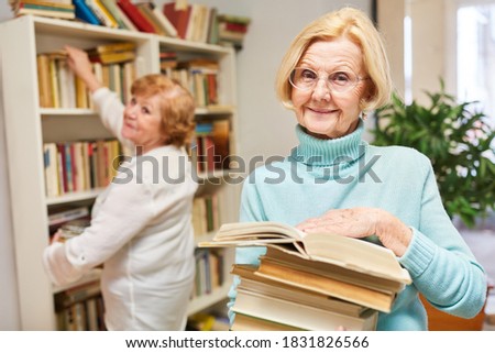 Smiling senior woman with a stack of books in the library for knowledge and training