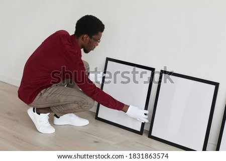High angle view at African-American man setting up blank black frames on floor while planning art gallery or exhibition, copy space