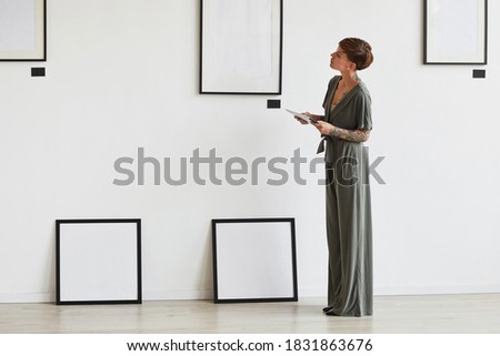 Graphic full length portrait of elegant female art gallery manager looking at frame setting while planning exhibition or event, copy space