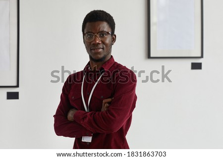 Waist up portrait of young African-American man looking at camera with arms crossed while working at art gallery or exhibition, copy space