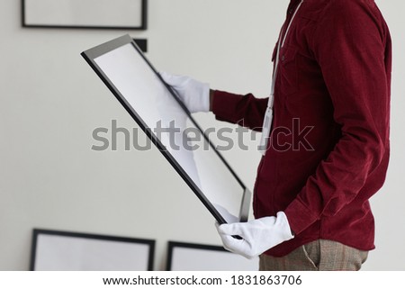 Cropped portrait of unrecognizable man wearing gloves holding painting frame while standing against white wall in art gallery, copy space