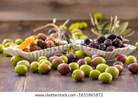 Green, black olives inside and outside in white bowl on wooden background.