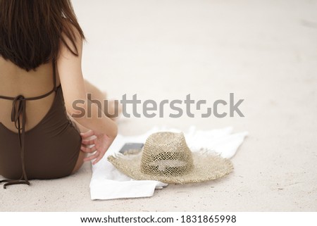 summer holiday concept, a girl set back on the beach, brown bikini, straw hat,