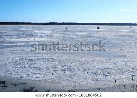 People of all ages walk on ice covered with snow and fish in winter, on a weekend, on a frozen river. Winter holidays, winter landscape