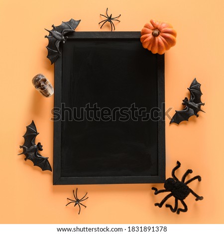 Halloween blank or invitation with party decorations, pumpkins, bats, skulls, spooky spider on orange background. Overhead view. Square composition. Copy space on chalkboard.