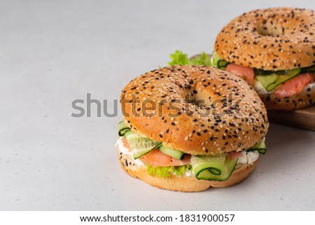 Bagels with smoked salmon, cream cheese, salad and cucumber. Light grey background. Copy space.