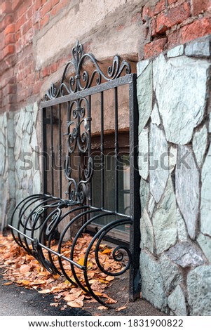 decorative metal grating on the basement window on the facade of the building, autumn leaves under it