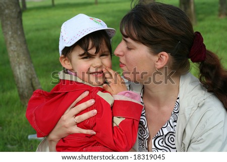 little girl with her mother in the spring park kissing