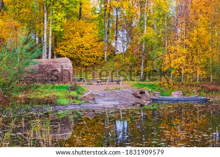 Dugouts canoes and a grass hut at a forest lake with autumn colors