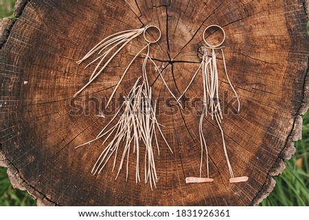 Idea with wedding gold rings. Homemade newlyweds made of pine needles, straw hold hands against the background of a wooden stump and green grass. Funny picture, concept, copy space.