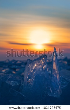 Glowing small figurines of broken ice on sky background during sunset, vertical winter landscape, closeup view