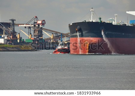 Large crude oil tanker ship pumping out ballast water when coming into port in Rotterdam, tug boat pushing the side Royalty-Free Stock Photo #1831933966