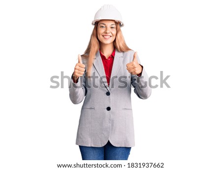 Beautiful young woman wearing architect hardhat success sign doing positive gesture with hand, thumbs up smiling and happy. cheerful expression and winner gesture. 