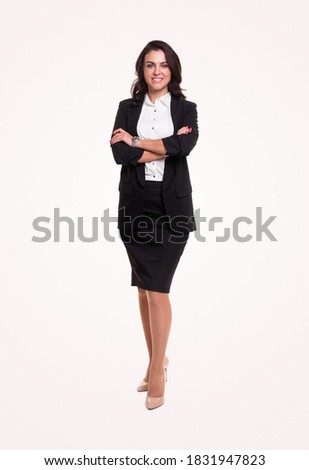 Full body of modern adult executive female manager in elegant formal black suit standing with arms crossed, against white background and looking at camera with smile