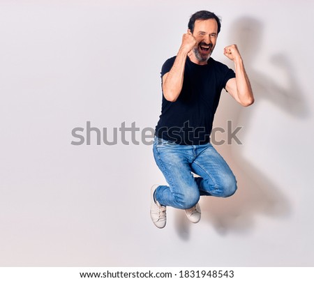 Middle age handsome man wearing casual clothes smiling happy. Jumping with smile on face doing winner gesture with fists up over isolated white background