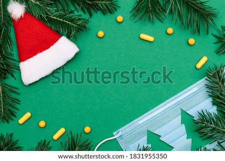 Frame made of Santa Claus hat,medical protective mask,Fir tree branches and yellow pills on the green background.Christmas, Happy New Year,coronavirus and medical concept.Copy space, flat lay