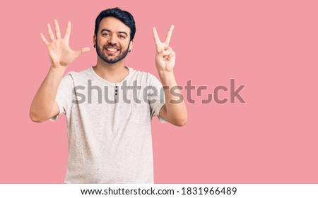 Young hispanic man wearing casual clothes showing and pointing up with fingers number seven while smiling confident and happy. 