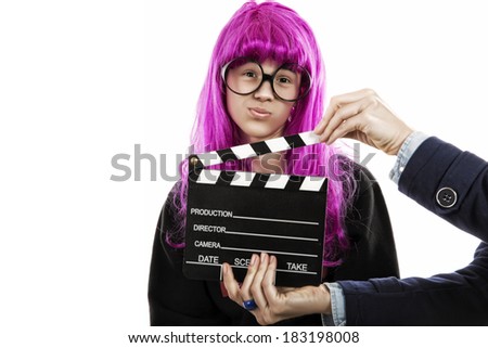 boy dressed as a woman with large glasses and pink wig. Woman hands holding a slate of films. humorous photo