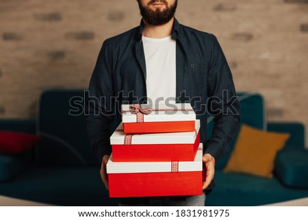 Man with beard holding white-red gift boxes. Surprise. Holiday and special occasion.