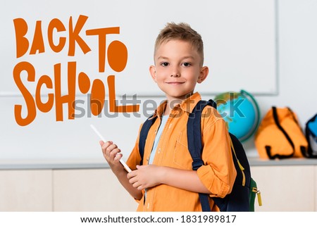 Schoolboy holding digital tablet near back to school illustration