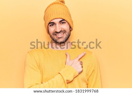 Young handsome bald man wearing sweater and wool cap smiling cheerful pointing with hand and finger up to the side 