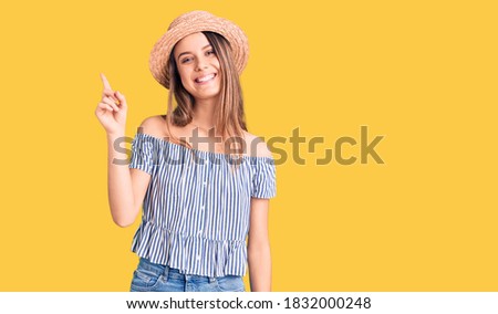 Young beautiful girl wearing hat and t shirt with a big smile on face, pointing with hand and finger to the side looking at the camera. 