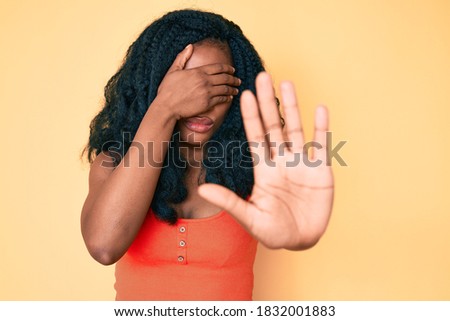 Beautiful african woman wearing casual clothes covering eyes with hands and doing stop gesture with sad and fear expression. embarrassed and negative concept. 